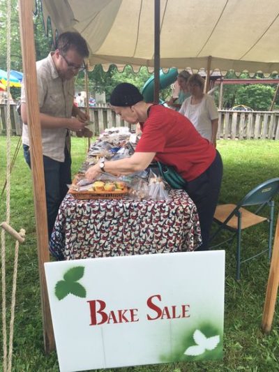 two people lean over a table of baked goods with a bake sale sign