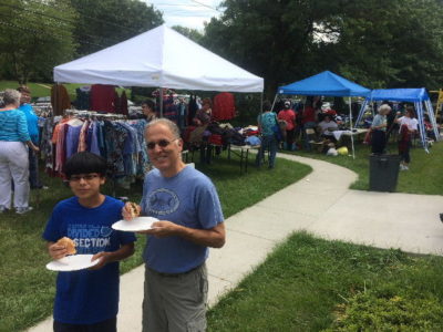 father and son eat hot dogs in front of tents full of racks of clothes